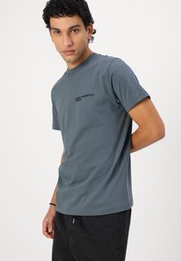 Grå kortärmad t-shirt i mjuk bomull. Har en svart logotyp "KARL LAGERFELD JEANS" på vänster bröst. Avslappnad passform.