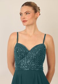 Teal jurk met een met pailletten versierde lijfje met gebogen patronen en dunne bandjes. Vloeiende rok die uit een aansluitende taille komt.