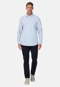 Camicia button-up azzurro chiaro con un delicato motivo a righe verticali, abbinata a pantaloni blu scuro e sneaker beige. Tessuto liscio e colletto classico.