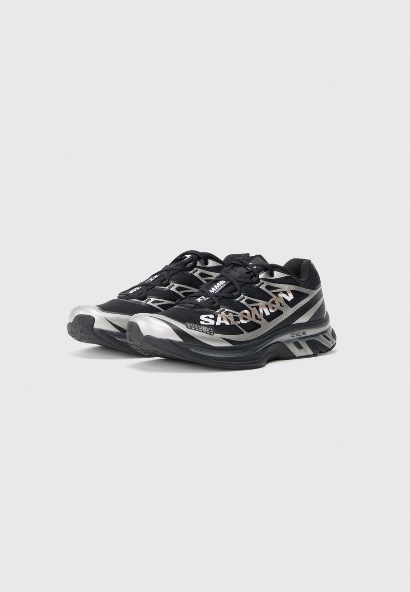 Black athletic shoes with silver accents. Mesh upper for breathability, textured sole for grip, featuring a cushioned midsole for comfort.