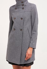 Abrigo de lana gris con cuello alto, diseño de doble botonadura y botones oscuros. Cuenta con bolsillos laterales y una silueta recta.