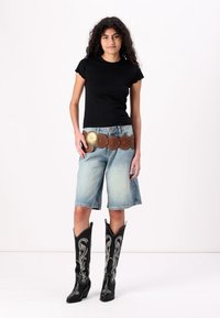 Μαύρο εφαρμοστό μπλουζάκι, ανοιχτό μπλε τζιν σορτς, καφέ κυκλική ζώνη με μεταλλικές λεπτομέρειες και μαύρες καουμπόικες μπότες με λευκή ραφή.