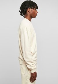Cremefarbener Sweatshirt aus weichem Stoff mit Rundhalsausschnitt, gerippten Bündchen und lockerer Passform. Keine sichtbaren Muster oder Logos.
