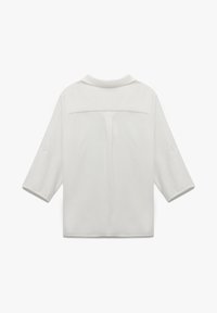 Camisa blanca con cuello, mangas tres cuartos y un detalle en el yugo en la parte posterior. La tela parece suave con un corte holgado. Sin patrones visibles.
