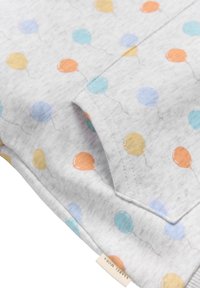 Tejido gris claro con un patrón de globos coloreados en naranja, azul y amarillo. Incluye una costura visible y una etiqueta en la esquina.