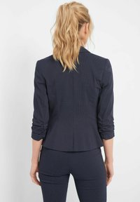 Granatowa dopasowana marynarka z marszczonymi rękawami i wzorzystą teksturą, z prostym tyłem i nowoczesną sylwetką.