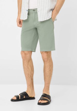 Light green shorts made of a soft, lightweight fabric. Includes front pockets and a button closure, paired with black slide sandals.