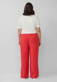 Weißes kurzärmliges Oberteil kombiniert mit roten weit geschnittenen Hosen. Die Hosen haben Gesäßtaschen und eine glatte Textur, während weiße Sneakers das Outfit abrunden.