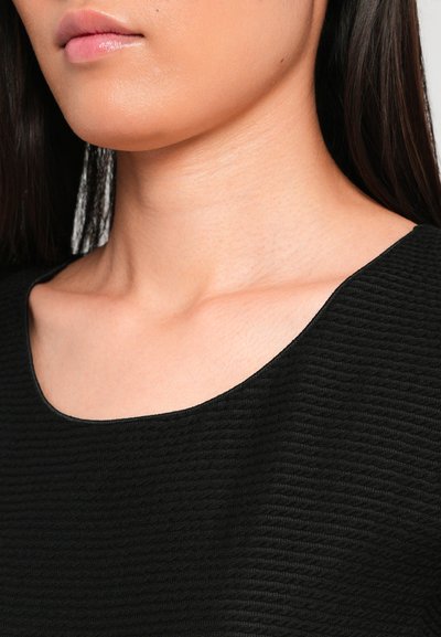 Black textured top with a round neckline, featuring subtle ribbing and soft fabric, showing part of a neck and shoulder area.