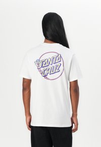 White cotton t-shirt featuring a colorful "Santa Cruz" graphic on the back, with a design of an alien and fire elements. Short sleeves.