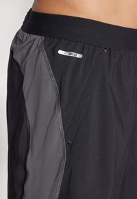 Schwarze sportliche Shorts mit grauen Seitenpanelen und elastischem Bund. Mit kleinem "ACTIBREEZE"-Logo in der Nähe des Bundes. Glatte Textur.