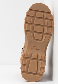 Semelle de chaussure en caoutchouc marron avec un motif de grip texturé, présentant des crampons profonds et un design rectangulaire. Marquée "MONKL" et taille "38".