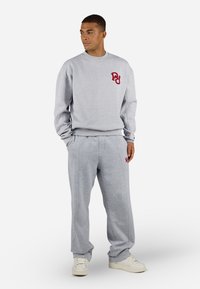 Gray sweatshirt and sweatpants set, featuring a red logo on the chest and pants. Fabric is soft with a relaxed fit and ribbed cuffs.