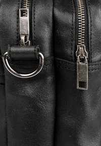 Schwarze Lederhandtasche mit zwei silbernen Reißverschlüssen und einem silbernen D-Ring. Auffällige, strukturierte Oberfläche und ordentlich genähte Kanten.
