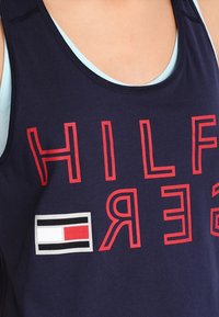 Canotta navy in cotone, con lettering rosso audace e un piccolo logo con accenti rossi, bianchi e neri. Design con collo a giro.