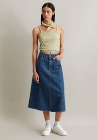 Light green cropped tank top paired with a blue denim midi skirt. The skirt features a button fly and pockets, worn with white sneakers.