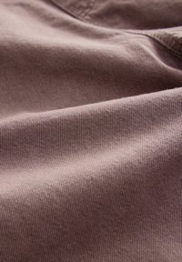 Gros plan d’un tissu doux brun violacé montrant une texture fine en maille et des plis délicats avec des coutures visibles.