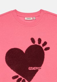 Růžová mikina s velkým tmavě burgundským chlupatým srdcovým vzorem. Má zaoblený výstřih a měkkou texturu. Štítek uvádí "ONLY."
