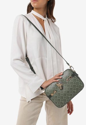 Borsa a tracolla verde con motivo, di forma rettangolare, dettagli hardware dorati e una singola tracolla regolabile, indossata incrociata su una camicia bianca.