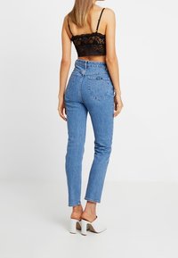 Jean en denim bleu taille haute avec une silhouette ajustée et des poches arrière, associé à un crop-top en dentelle noire et des sandales blanches à talons.