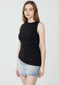 Zwarte geribbelde mouwloze top gecombineerd met een lichtblauwe denim minirok. Gladde textuur, aansluitend ontwerp met een ronde zoomlijn.