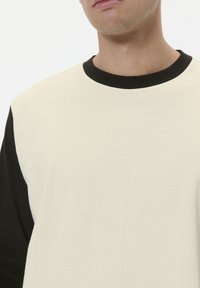 Crème lange mouw t-shirt met zwarte accenten op de schouders en een zwarte ronde halslijn, gemaakt van zachte, lichte katoen.