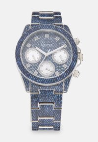 Reloj azul y plateado con un patrón de denin texturizado, tres subesferas y marcadores horarios similares a diamantes. Pulsera de acero inoxidable con acabado pulido.
