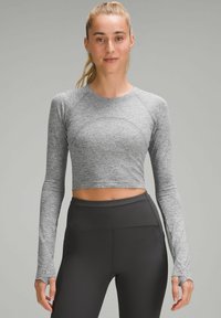 Graues Langarm-Crop-Top mit tailliertem Design, Raglanärmeln und Daumenlöchern, kombiniert mit schwarzen, hoch geschnittenen Leggings.