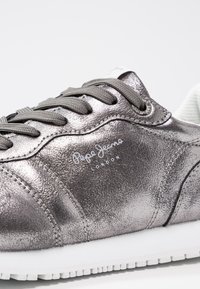 Metaliczne szare trampki Pepe Jeans z szarymi sznurowadłami, białą podeszwą i teksturowaną skórzaną powierzchnią, z logo marki po boku.
