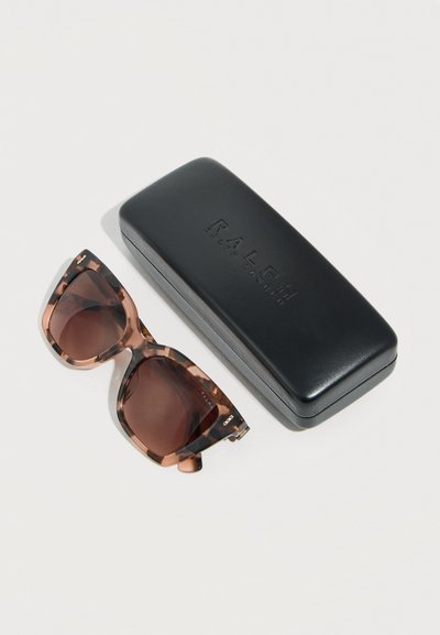 Γυαλιά ηλίου με σχέδιο χελώνας και καφέ φακούς δίπλα σε μαύρη δερμάτινη θήκη για γυαλιά ηλίου Ralph Lauren πάνω σε λευκή επιφάνεια.