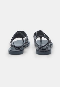 Zwarte sandalen met kruislings gespen, voorzien van zilveren studs, een platte zool en een open achterkant voor ventilatie en gemak bij het dragen.