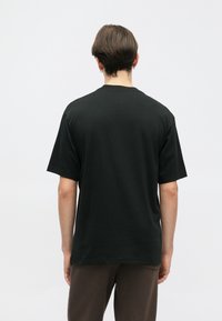 Schwarzes Baumwoll-T-Shirt mit lockerer Passform, kurzen Ärmeln und Rundhalsausschnitt; glatte Textur, einfaches Design ohne Muster oder Akzente.