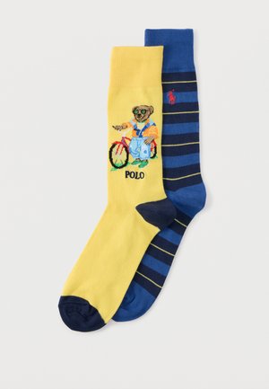 Κίτρινη κάλτσα με μια αρκούδα που φοράει γυαλιά ηλίου και φορμάκι δίπλα σε κόκκινο ποδήλατο με την επιγραφή "POLO", σετ με μια μπλε κάλτσα με σκούρες μπλε και κίτρινες ρίγες.