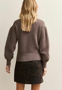 Suéter marrón de punto con mangas abullonadas, dobladillo acanalado, combinado con una falda corta con un patrón de estampado de leopardo.