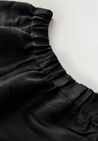 Svart satintyg med detalj av rynkad halsringning, visar en slät textur och subtil glans. Närbild av tygens fall och veck.