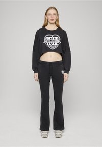 Czarny krótki top z białym nadrukiem graficznym, zestawiony z czarnymi rozkloszowanymi dresami. Tkanina wydaje się miękka; wyróżnia się luźny krój i detale stylistyczne stroju.