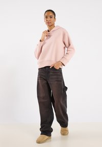 Felpa con cappuccio rosa a vestibilità rilassata, jeans neri larghi e scarpe beige senza lacci. Tessuto morbido, design semplice e dettagli minimi.