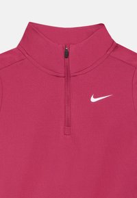 Obopnutý športový top na zips v tmavo ružovej farbe s vysokým golierom. Obsahuje malé biele logo Nike na hrudi a hladký, elastický materiál.