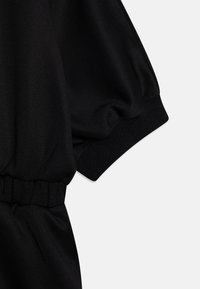 Czarny fragment odzieży z miękkiego materiału, z dużymi bufkami na rękawach, elastycznymi mankietami i pasem, prezentującym gładką, matową teksturę.