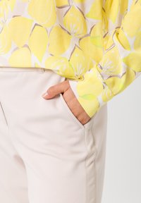 Geel, bloemenpatroon blouse met lange mouwen, gecombineerd met lichtbeige broek. De blouse heeft citroenen en bladeren en vertoont een gladde textuur.