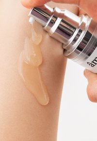 Klar pumpflaske, der dispenserer et gennemsigtigt, gel-lignende serum på huden. Glat, skinnende tekstur med et let gyldent skær.