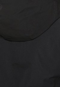 Gros plan de l'arrière d'une veste noire avec capuche, montrant la texture du tissu et les coutures cousues.