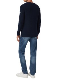 Marineblauer gerippter Pullover mit einem Rundhalsausschnitt und einem Logo-Patch auf dem linken Ärmel, kombiniert mit hellblauen geraden Jeans und weißen Sneakern.