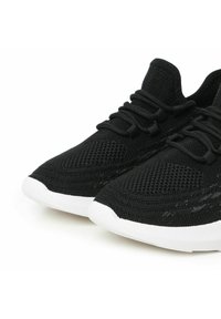 Scarpe da ginnastica nere con tomaia in rete testurizzata, lacci elastici e suola in gomma bianca. Design elegante con punta arrotondata.