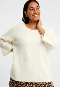 Cremefarvet, puffy sweater med rund hals og trekvartærmer. Blød tekstur og afslappet pasform, parret med en leopardmønsteret nederdel.