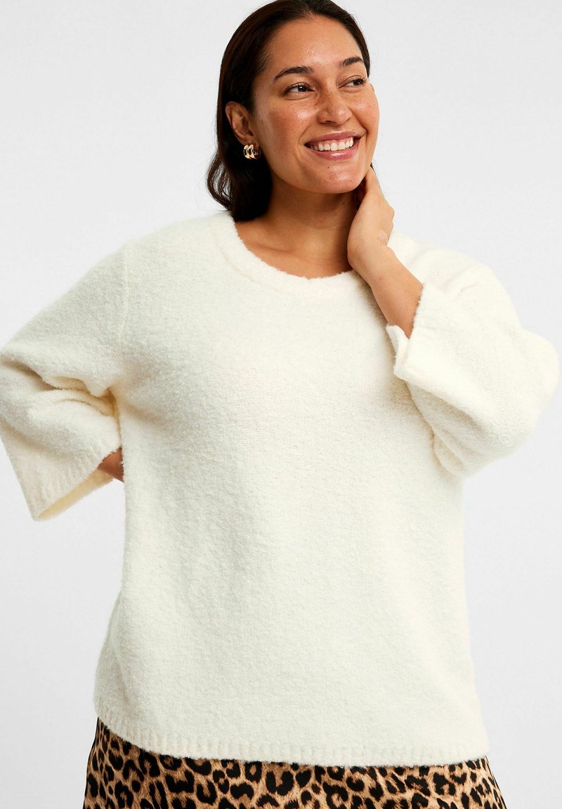 Cremefarvet, puffy sweater med rund hals og trekvartærmer. Blød tekstur og afslappet pasform, parret med en leopardmønsteret nederdel.