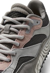 Baskets grises et noires avec tissu en maille, accents en daim rose clair, panneau noir texturé et motif de semelle distinctif. Les lacets sont gris clair.