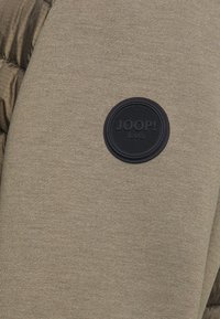 Khaki bomulds sweatshirt med en struktureret overflade og en cirkulær sort gummi logo-patch med teksten "JOOP! JEANS."
