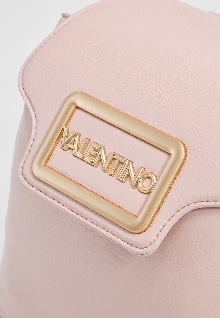 Rosa Handtasche aus Kunstleder mit einer goldenen rechteckigen Logo-Plakette, auf der "VALENTINO" eingestanzt ist. Glatte Textur und abgerundete Kanten.