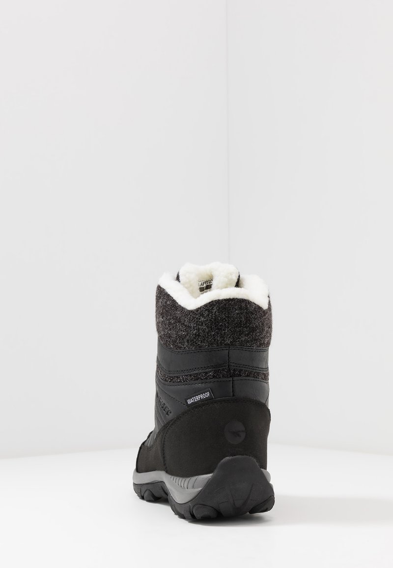 Bota impermeable negra con parte superior de fieltro gris, suave forro blanco en el cuello y suela de goma texturizada. Presenta un talón curvado para mayor soporte.